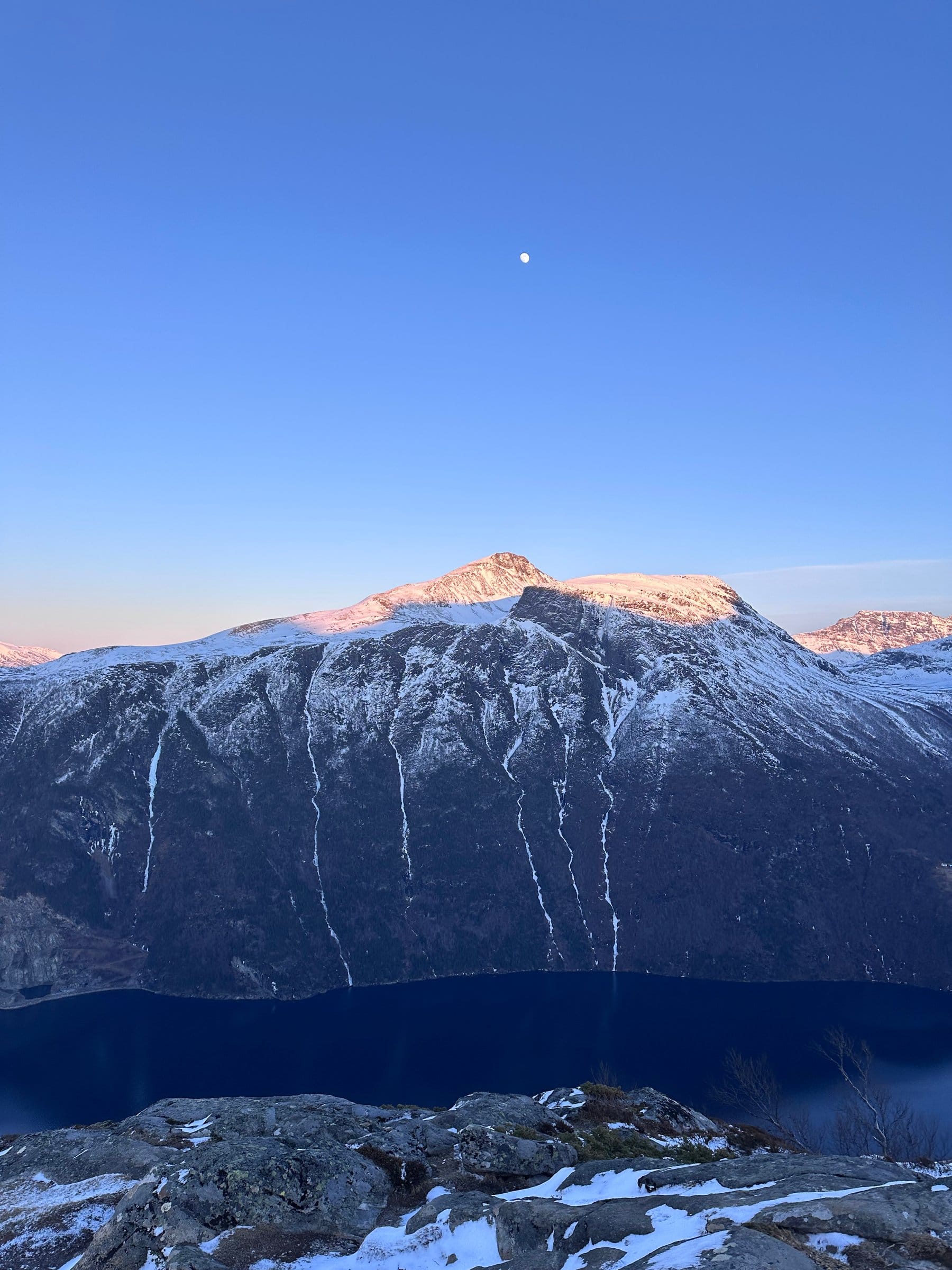 Måneopplyst utsikt fra Lievarden med snødekte fjellsider over en mørk fjord i solnedgang.