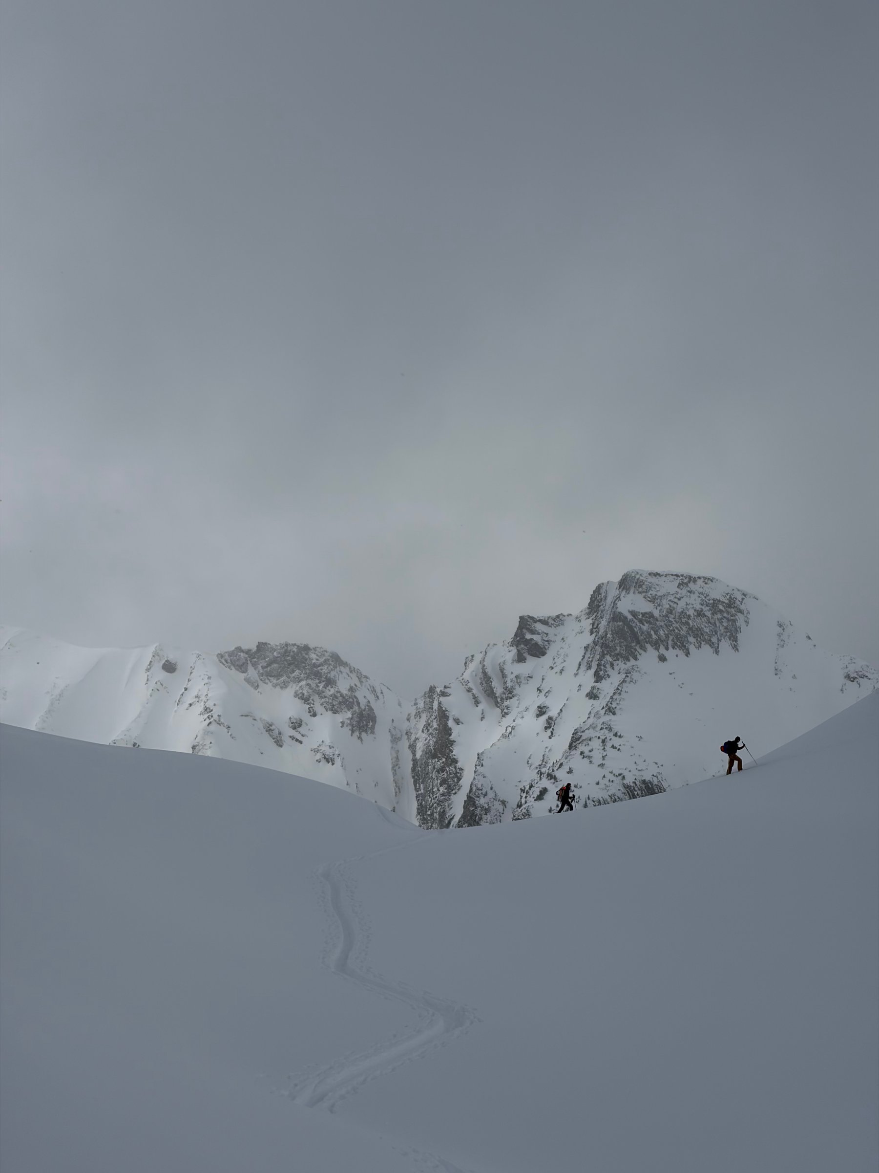 To toppturløpere på vei opp gjennom stemningsfullt alpint terreng med spor i nysnø